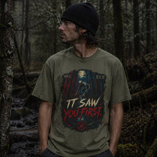 Man wearing a t-shirt with a graphic rake design in a forest setting