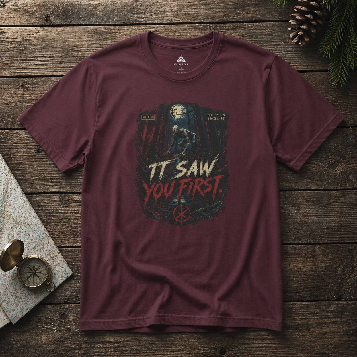 Maroon t-shirt with rake graphic design and text on a wooden surface