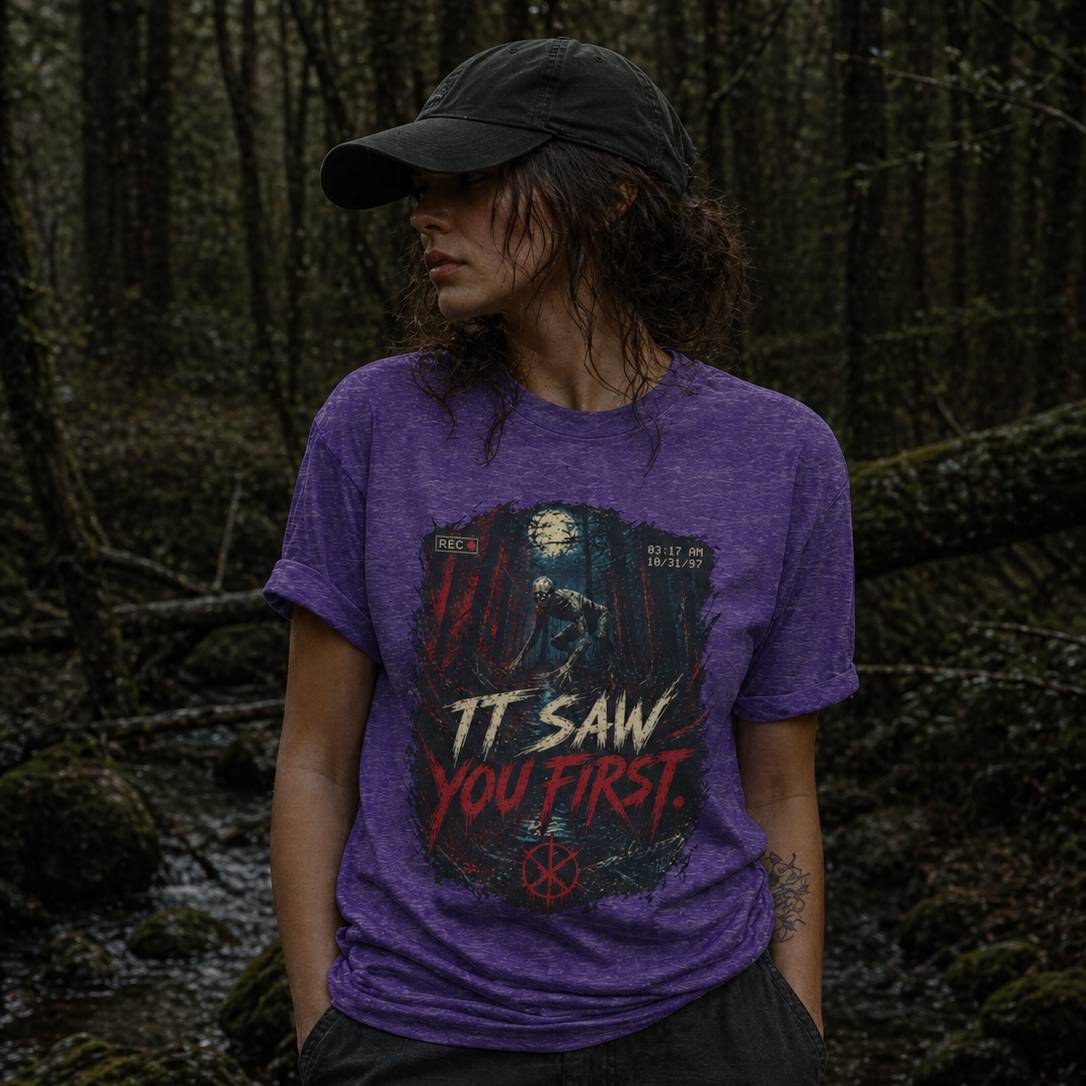 Person wearing a purple t-shirt with a rake graphic design and text in a forest setting