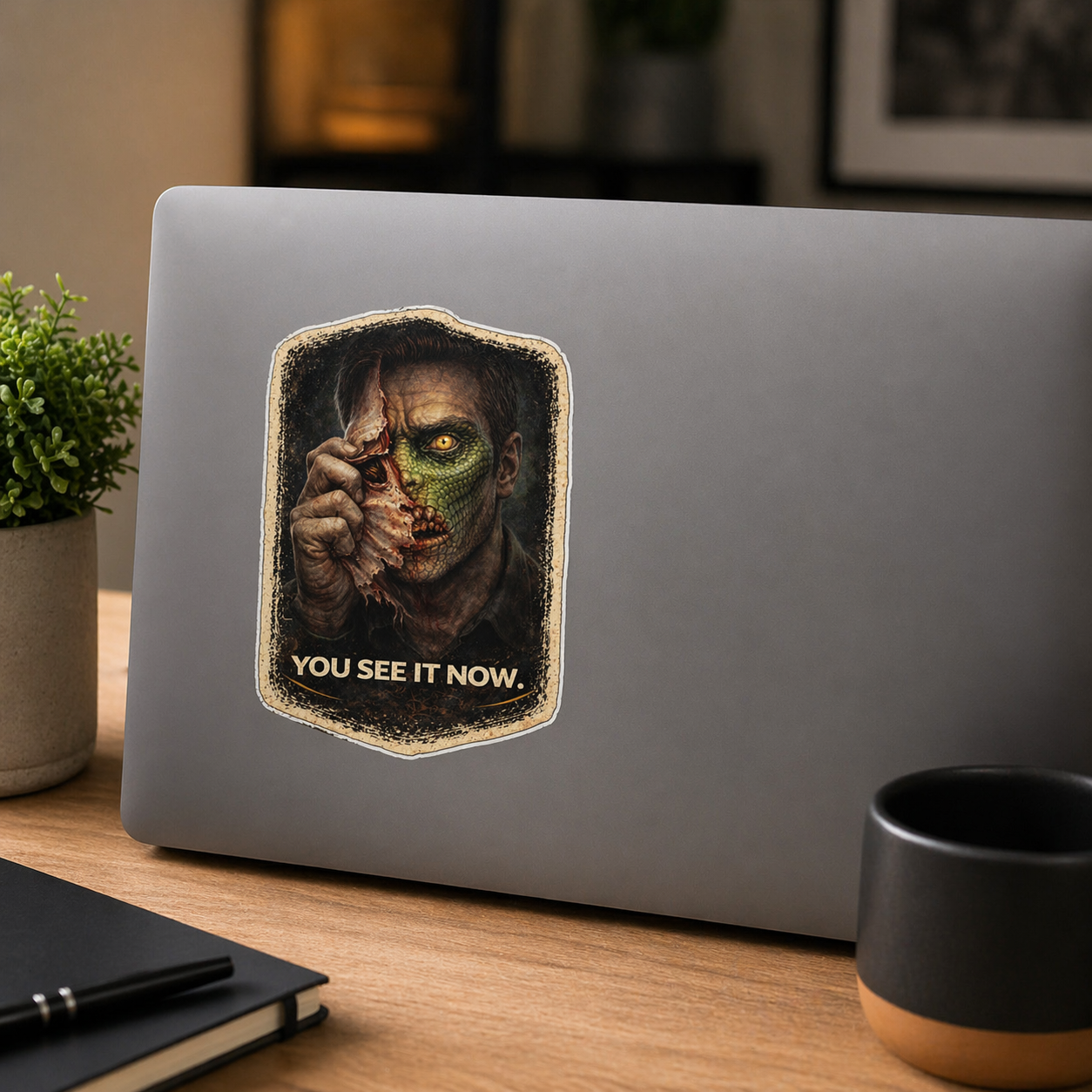 Laptop with a sticker of a character holding a knife and the text 'You See It Now' on a wooden desk.