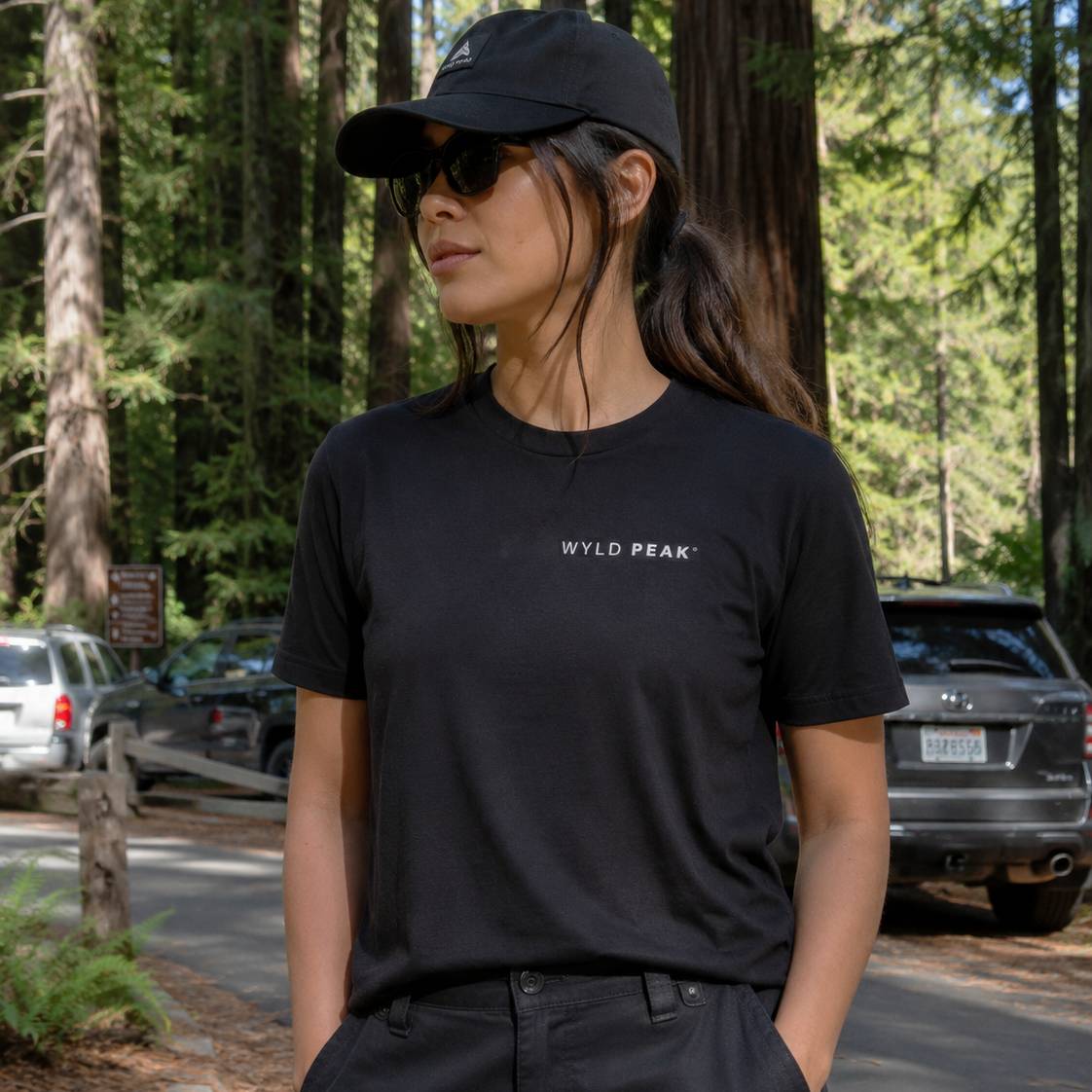Person wearing a black t-shirt with 'WYLD PEAK' logo in a forest setting