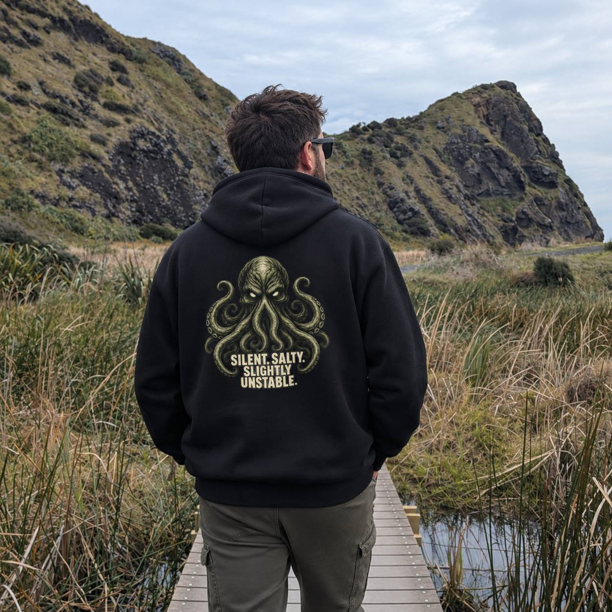 A man viewed from behind wearing a black hoodie with a large green octopus graphic and the text 'SILENT SALTY. Slightly Unstable.