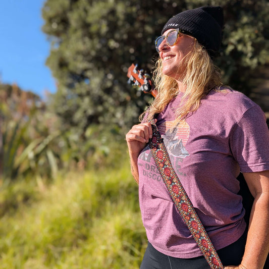 Front view of Sim Bastick in Wyld Peak Explorers eco tee with guitar at Matauri Bay NZ