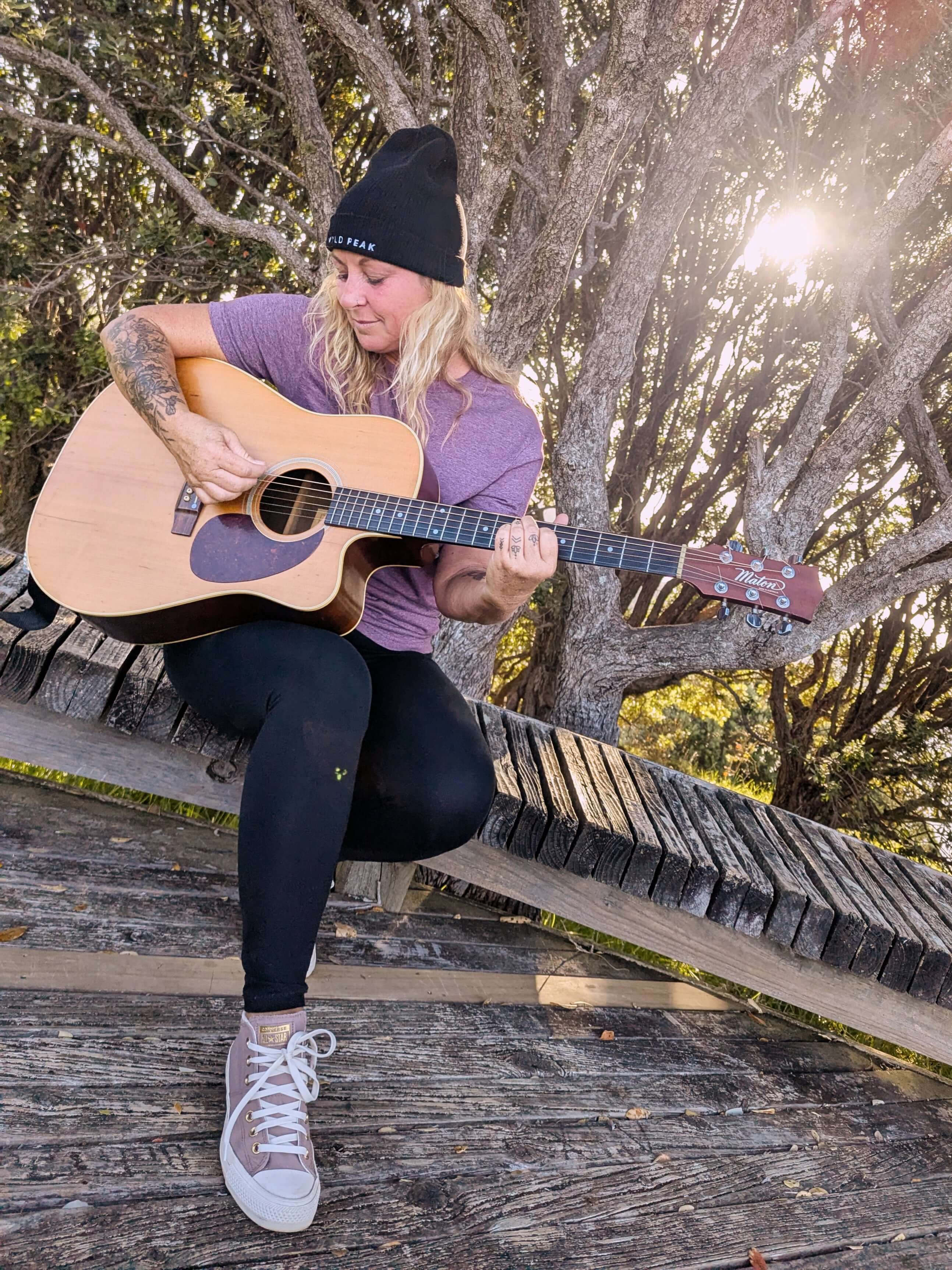 Sim Bastick playing guitar and singing in Wyld Peak maroon Explorers tee at Matauri Bay