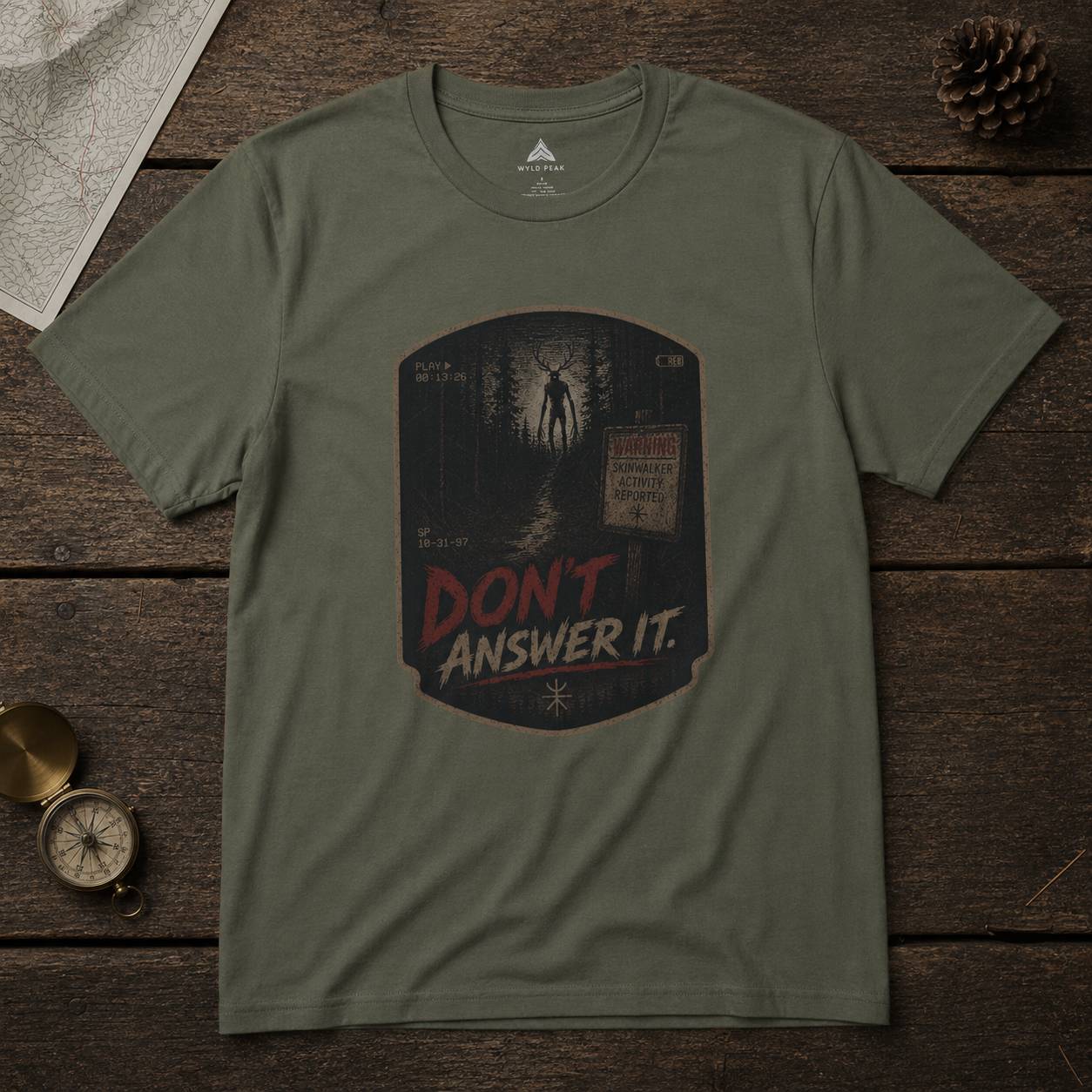 Green t-shirt with 'Don't Answer It' skinwalker graphic on a wooden surface