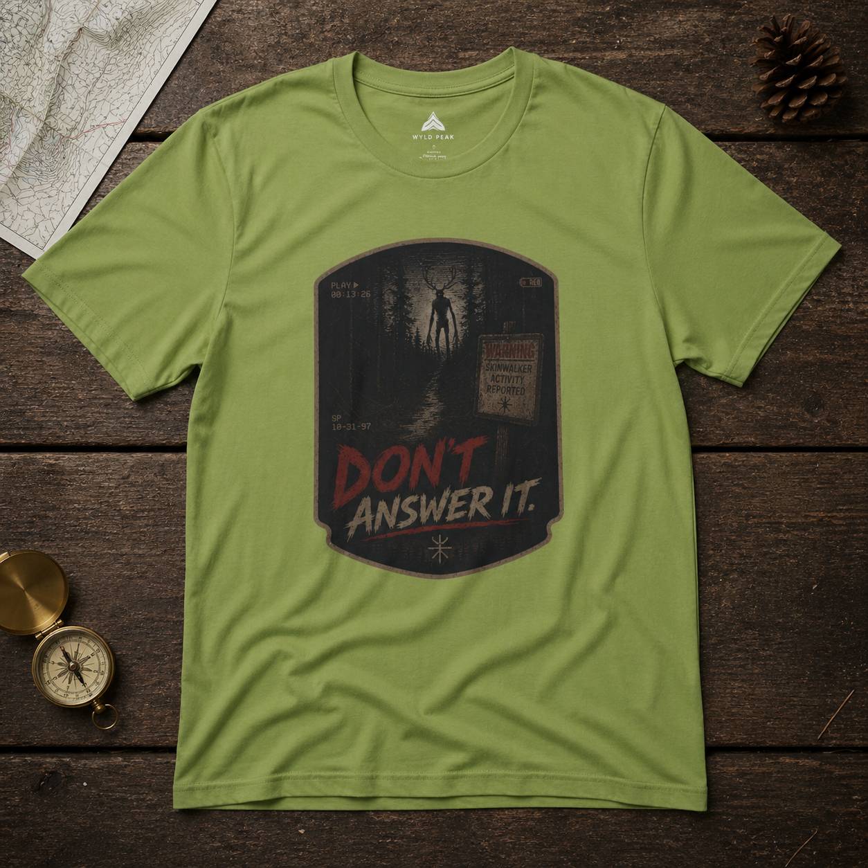 Green t-shirt with a skinwalker graphic design and text 'Don't Answer It' on a wooden surface.