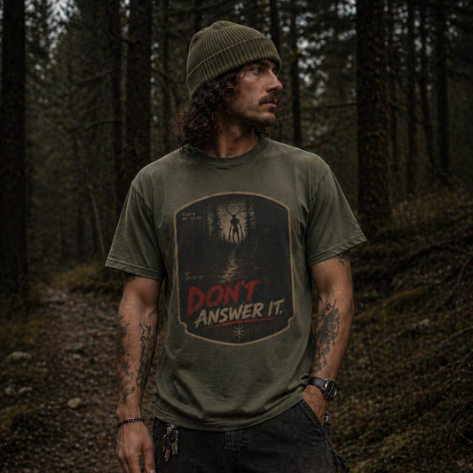 Man wearing a t-shirt with 'Don't Answer It' skinwalker graphic in a forest setting