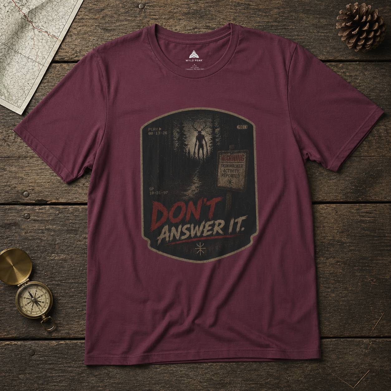 Maroon t-shirt with 'Don't Answer It' graphic on a wooden surface with map and compass.