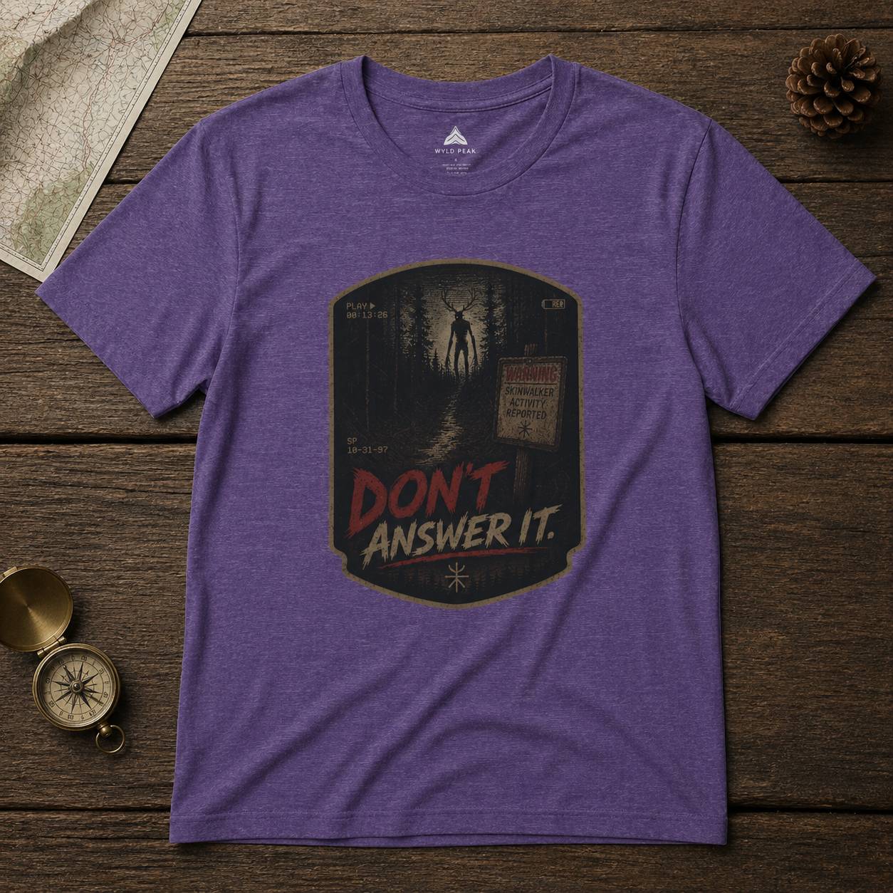 Purple t-shirt with cryptid graphic design and text 'Don't Answer It' on a wooden surface.