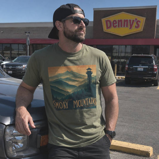 Man wearing a t-shirt with 'Great Smoky Mountains' design, standing next to a truck in front of a Denny's restaurant.