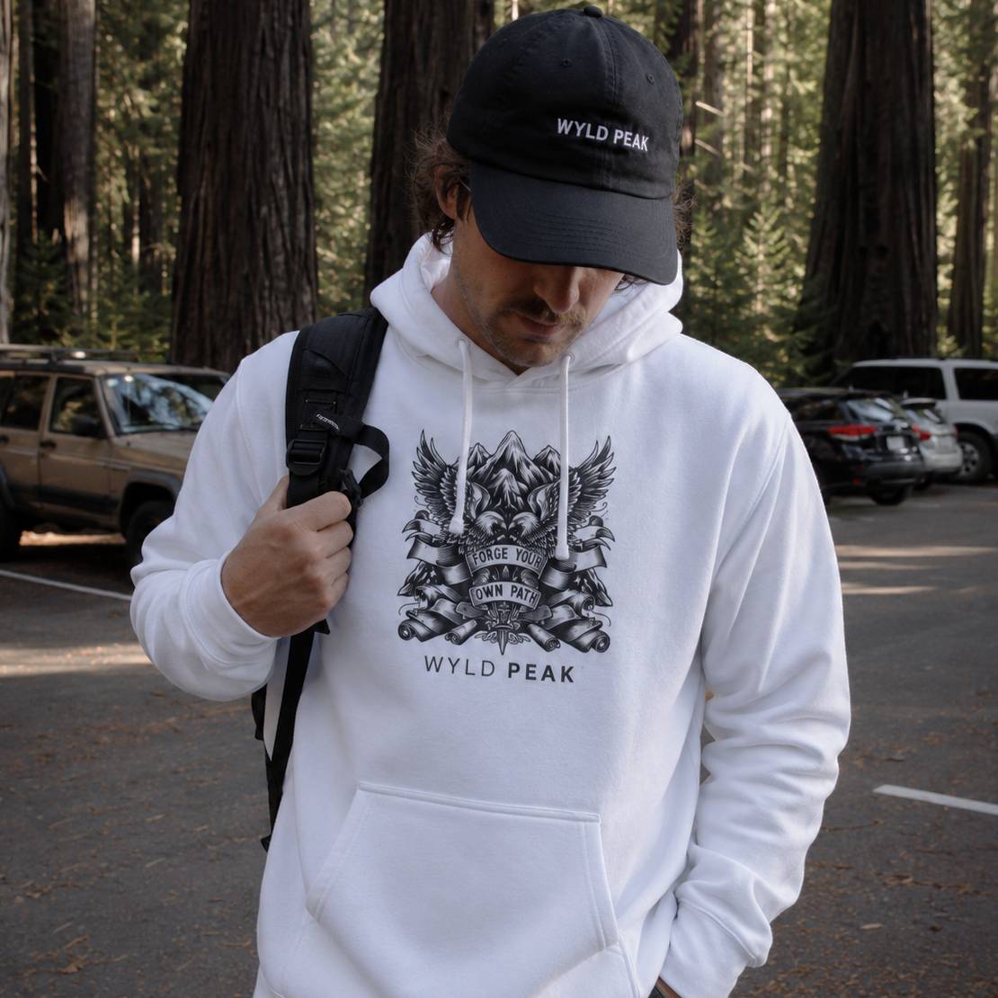 Person wearing a white hoodie and black cap with 'Wyld Peak' branding in a forest setting.