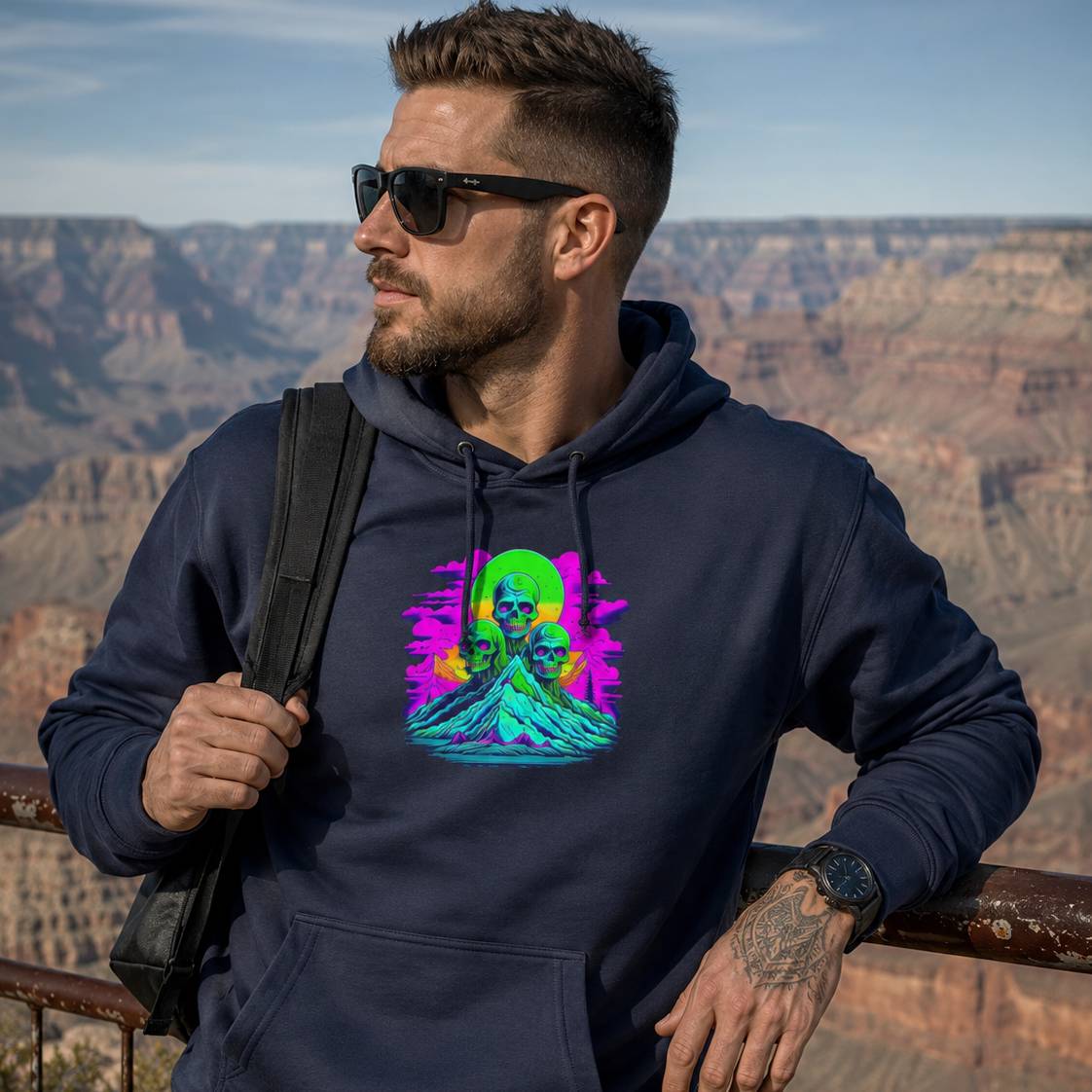 Man wearing a navy hoodie with a colorful graphic design, standing in front of a scenic landscape.