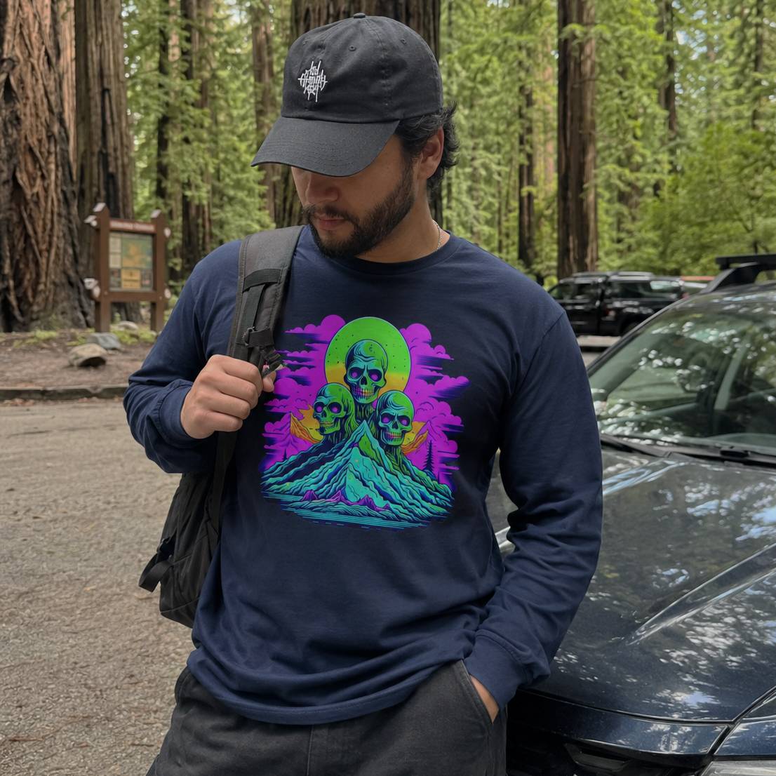 Man wearing a navy blue sweatshirt with a colorful graphic design, standing in a forested area.