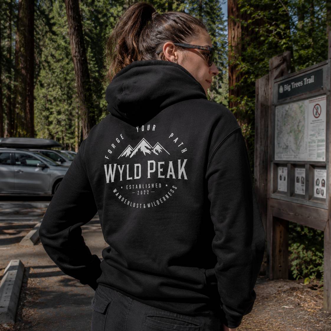 Person wearing a black hoodie with 'Wyld Peak' logo in a forest setting