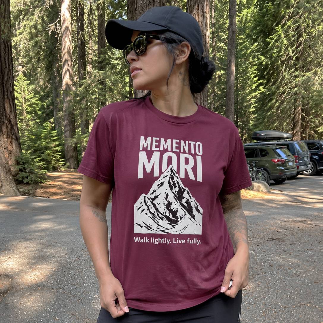 Person wearing a maroon t-shirt with a mountain graphic and text in a forest setting