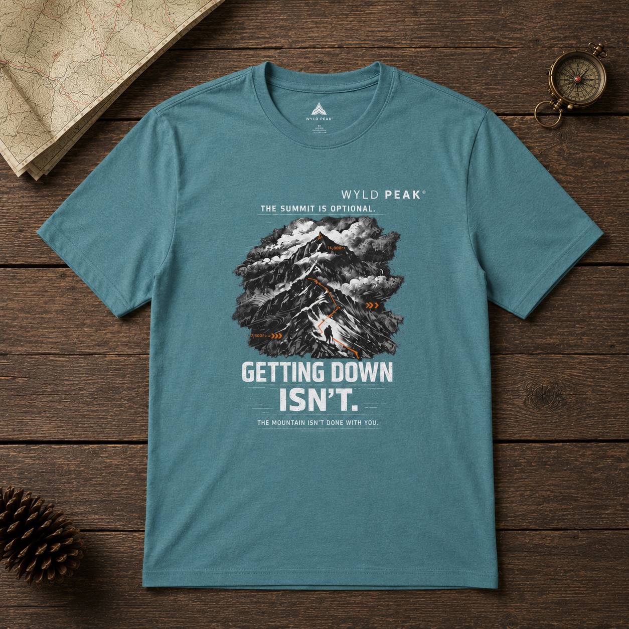 Teal t-shirt with mountain graphic and text on a wooden surface