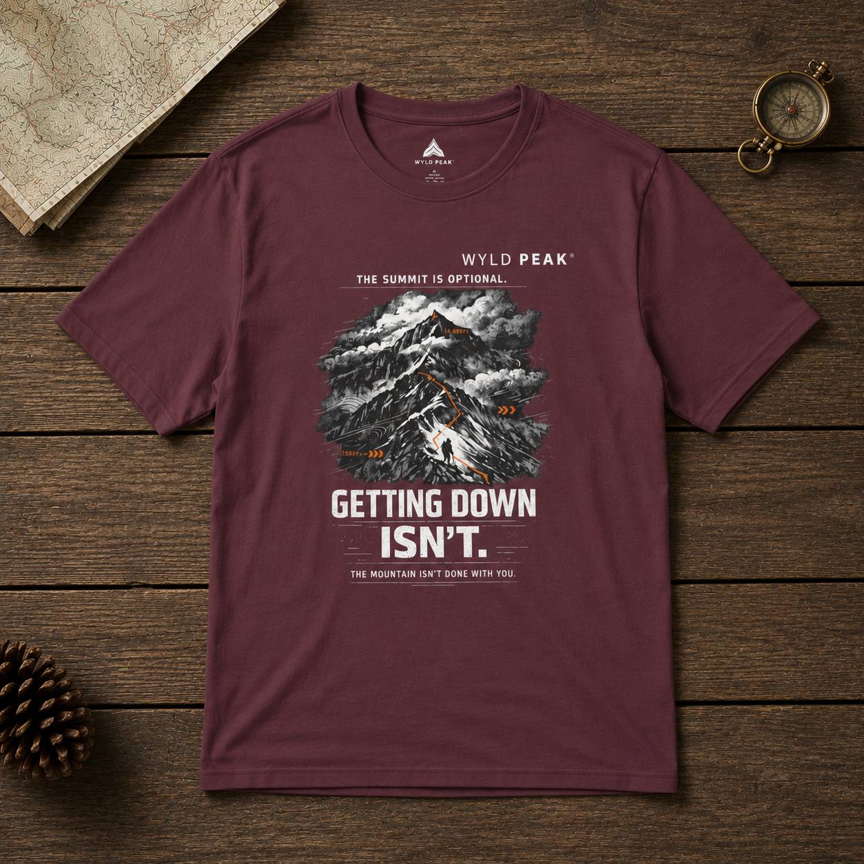 Maroon t-shirt with mountain graphic and text on a wooden surface