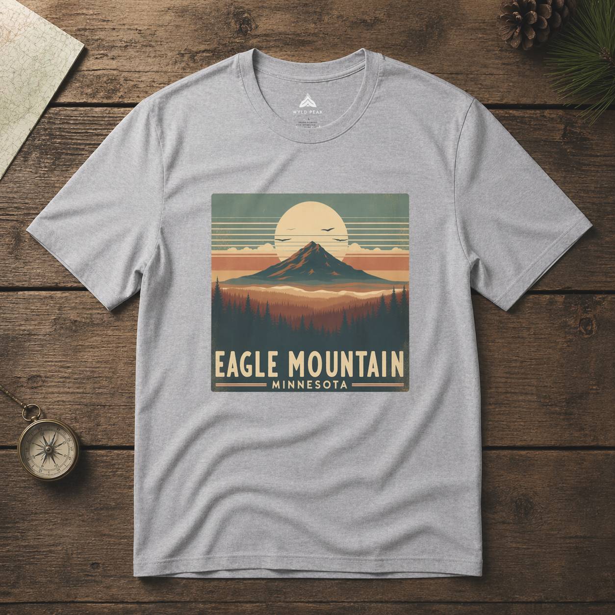 Gray t-shirt with 'Eagle Mountain, Minnesota' graphic on a wooden surface