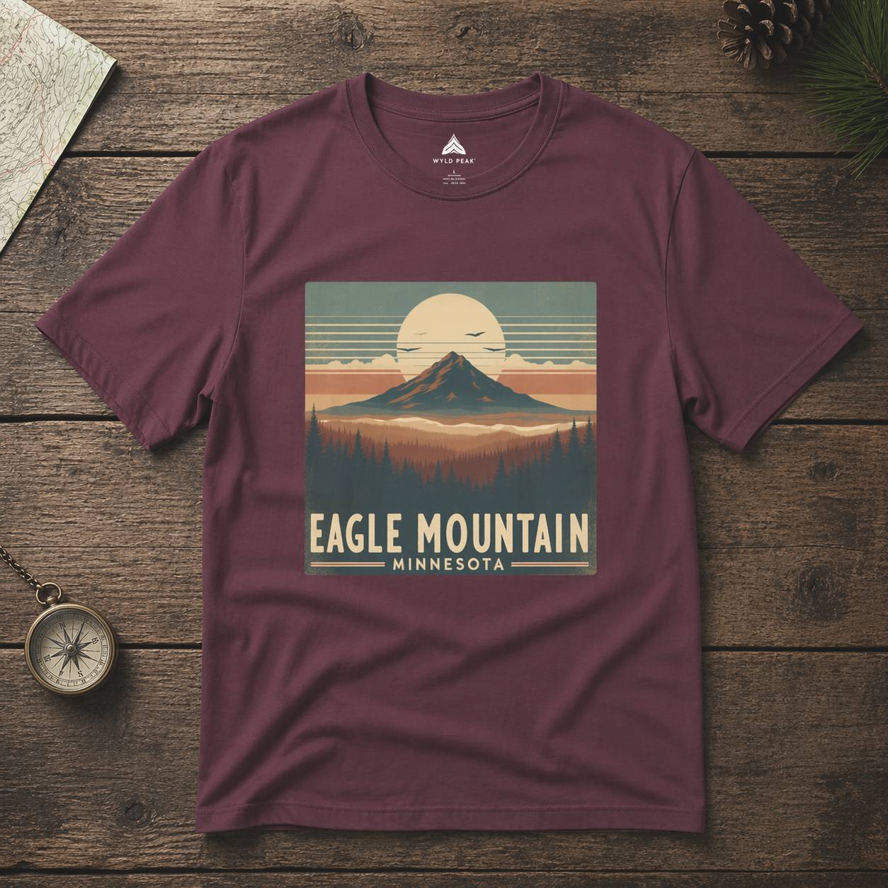 Maroon t-shirt with 'Eagle Mountain, Minnesota' graphic on a wooden surface