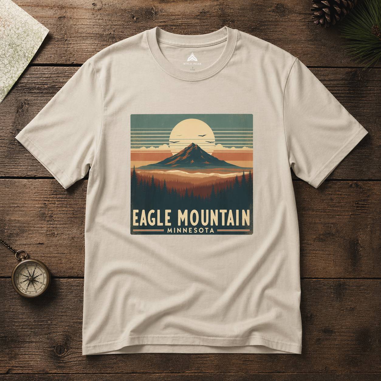 Beige t-shirt with 'Eagle Mountain, Minnesota' graphic on a wooden surface