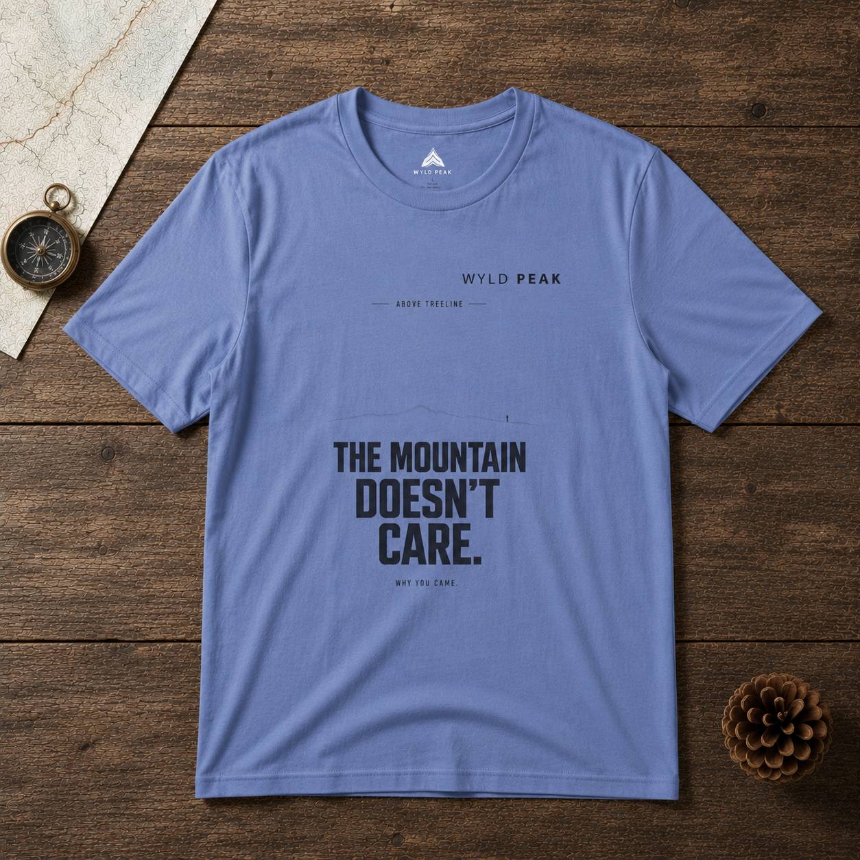 Blue t-shirt with 'The Mountain Doesn't Care' text on a wooden surface