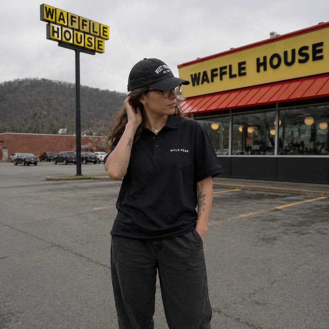 Person wearing a black cap and shirt in front of a Waffle House restaurant.