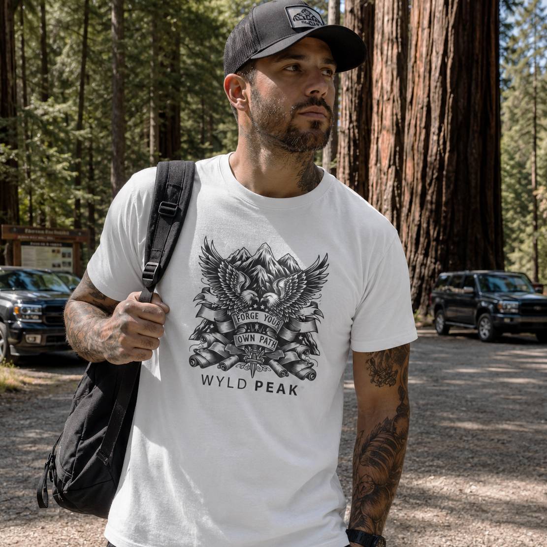 Man wearing a white t-shirt with an eagle design and 'Wyld Peak' text, standing in a forested area.