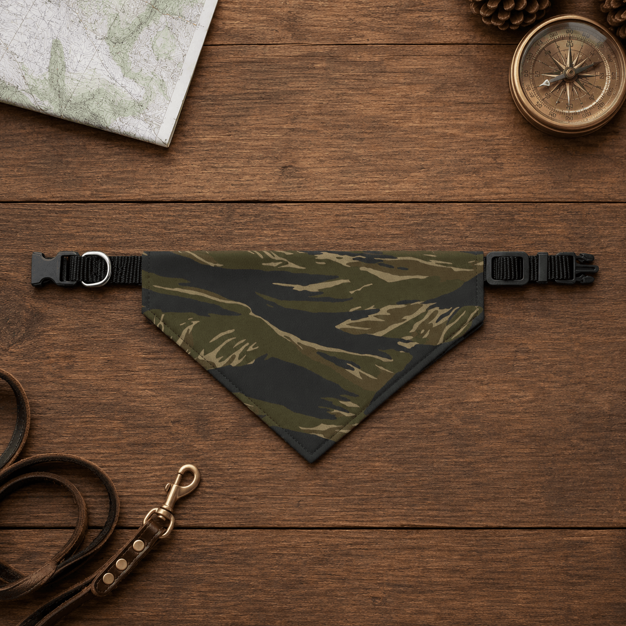 Camouflage dog bandana on a wooden surface with a leash and compass.