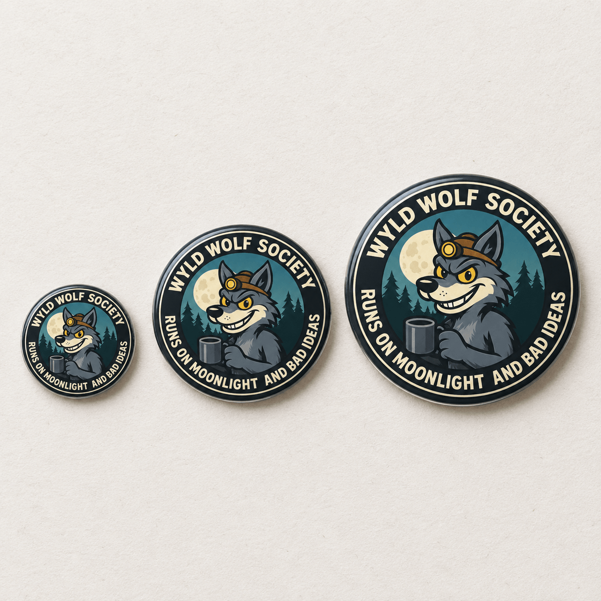 Three circular enamel pins of varying sizes arranged by size on a light beige textured background. The pins feature a cartoon gray wolf wearing a brown aviator hat and holding a dark gray mug, with a full moon and pine trees in the background.