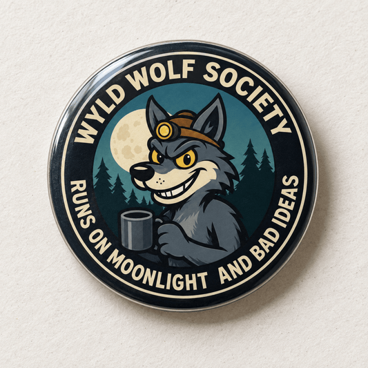 A circular enamel pin featuring a cartoon gray wolf wearing a brown headlamp and holding a mug, with a full moon and pine trees in the background. The pin has a black outer border with the text 'WYLD WOLF SOCIETY' and 'RUNS ON MOONLIGHT AND BAD IDEAS' in cream lettering.