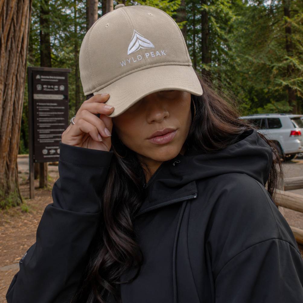 Person wearing a beige cap with 'Wyld Peak' logo in a forest setting