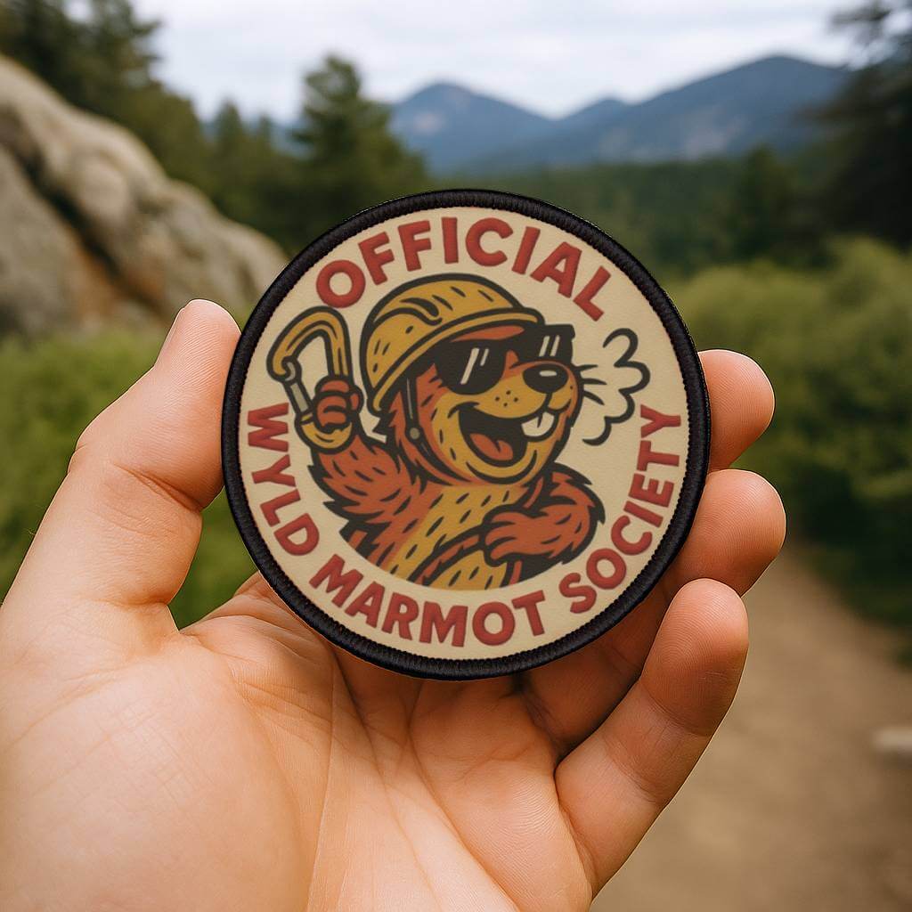 Wyld Peak Marmot Society patch being held on a scenic hiking trail
