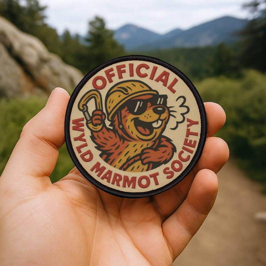 Wyld Peak Marmot Society patch being held on a scenic hiking trail