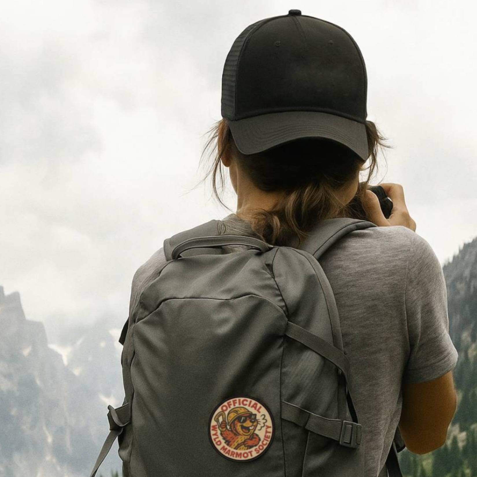 Hiker taking a photo on a trail with Wyld Peak Marmot Society patch on backpack
