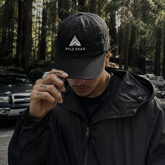 Person wearing a black cap with 'Wyld Peak' logo in a forest setting