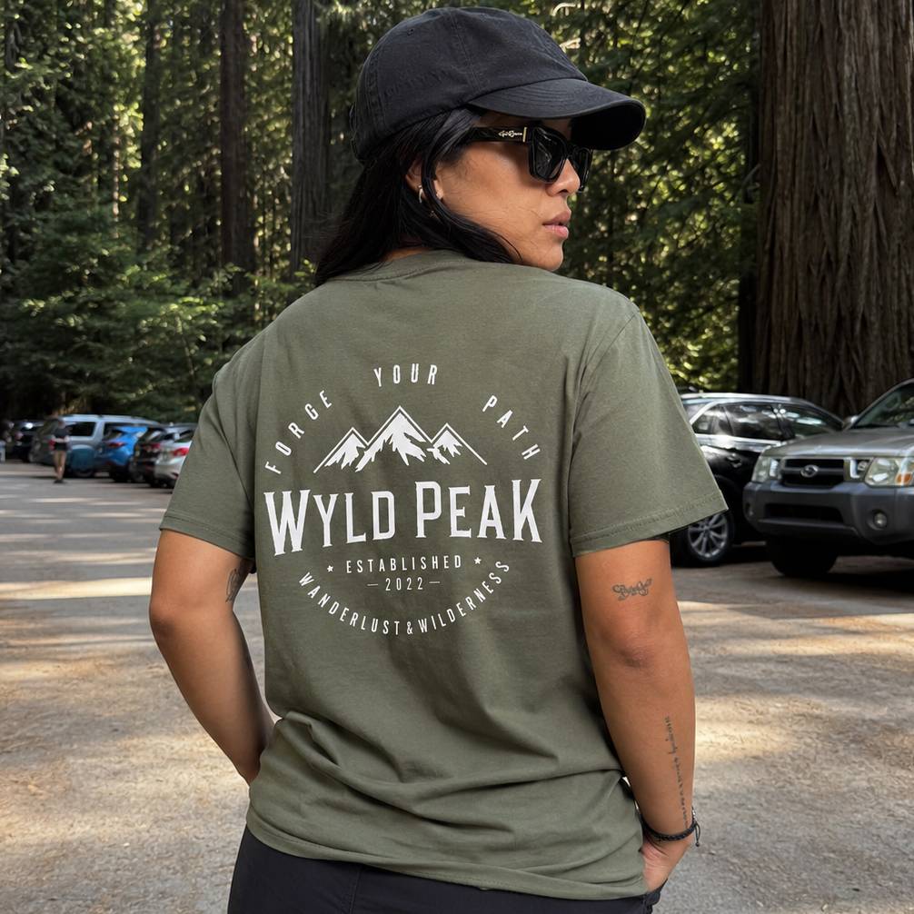 Person wearing a green t-shirt with 'Wyld Peak' branding in a forest setting