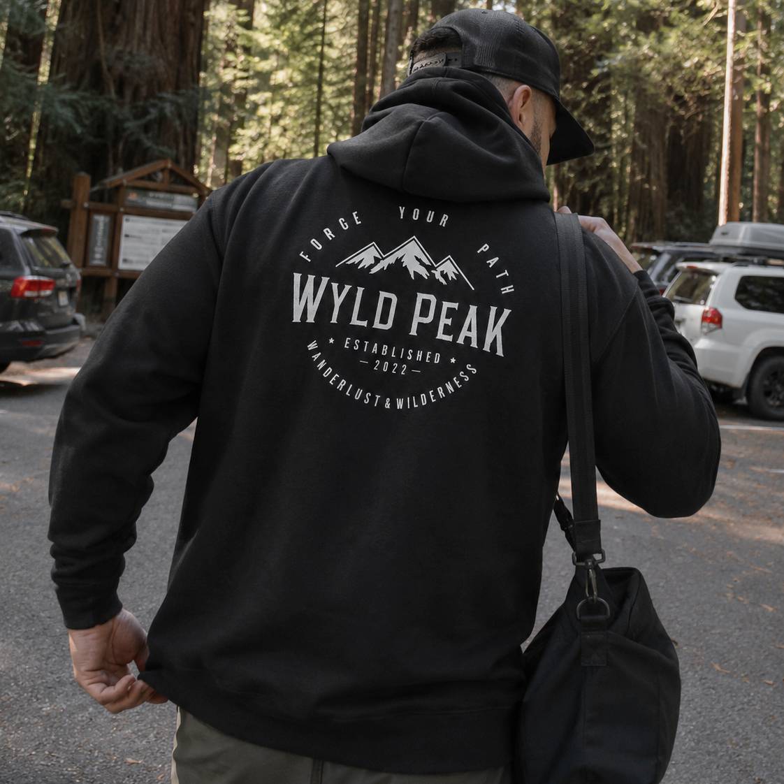 Person wearing a black hoodie with 'Wyld Peak' logo in a forest setting
