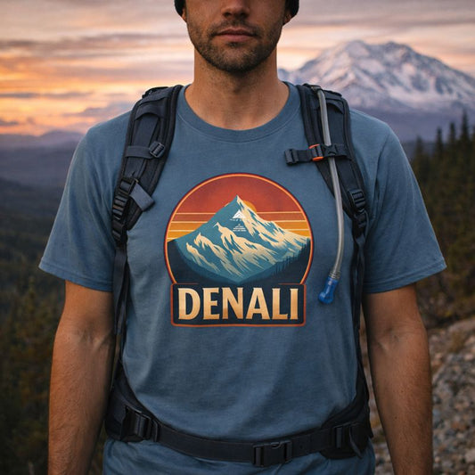 Person wearing a blue t-shirt with Denali mountain graphic and text, standing in front of a mountainous landscape.