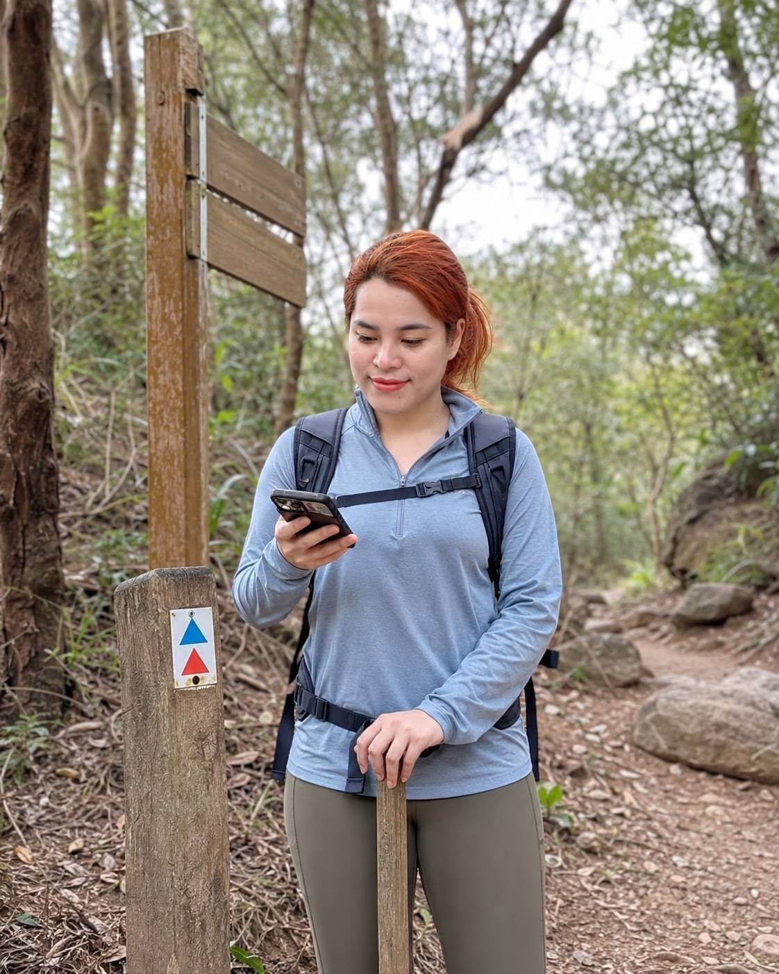Woman with a backpack using a phone in a forest setting