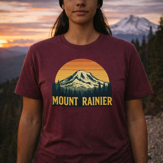Person wearing a maroon t-shirt with Mount Rainier graphic in a mountainous landscape