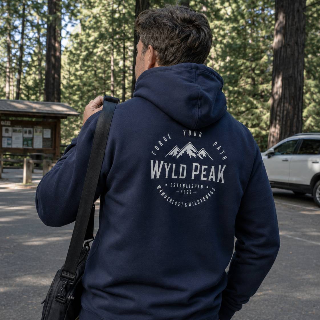 Person wearing a navy hoodie with 'Wyld Peak' logo in a forest setting