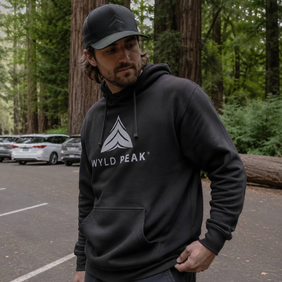 Man wearing a black hoodie with 'Wyld Peak' logo in a forest setting