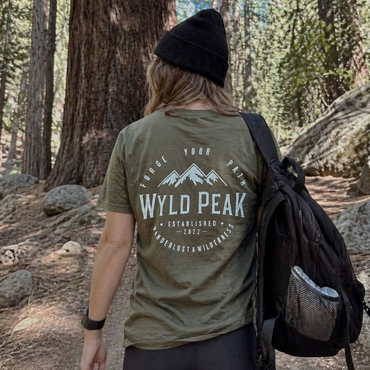 Person wearing a green 'Wyld Peak' t-shirt in a forest setting