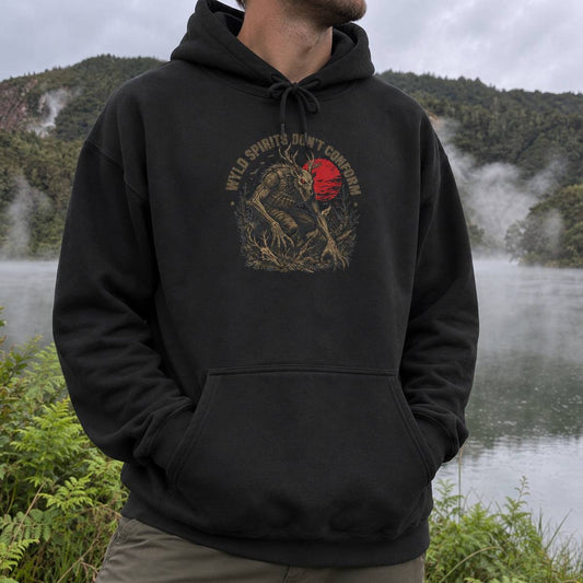 A man wearing a black pullover hoodie with a graphic print of a werewolf holding a red moon and the text 'WYLD SPIRITS DON'T CONFORM'. The background shows a misty lake and forested hills.