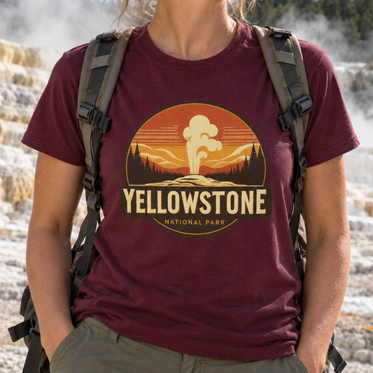 A person wearing a maroon t-shirt with a retro-style Yellowstone National Park graphic, carrying a hiking backpack in an outdoor geothermal setting.