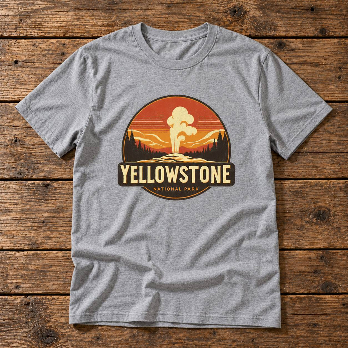 A heather gray short-sleeve t-shirt with a circular Yellowstone National Park graphic on the chest, laid flat on a rustic wooden plank background.