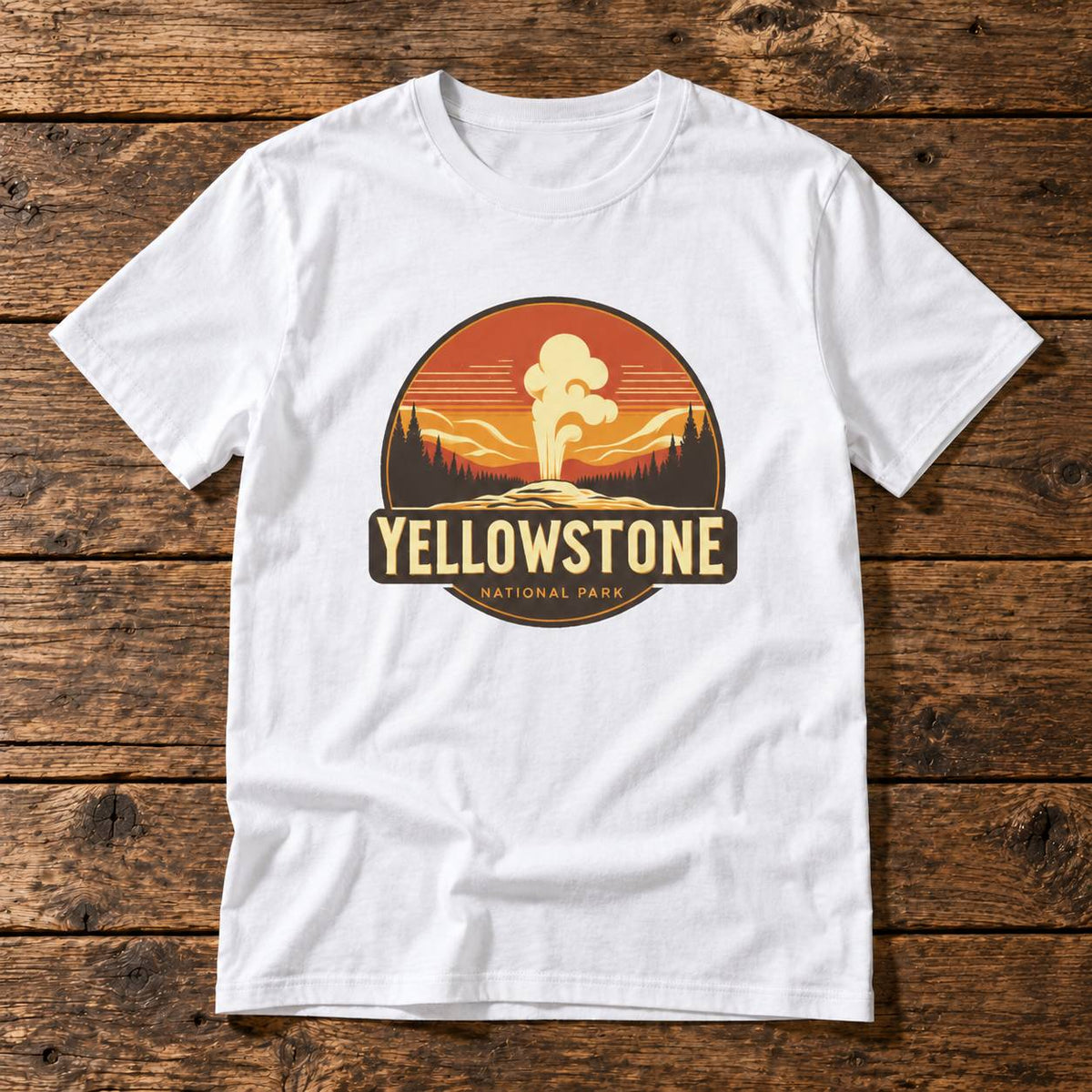 A white short-sleeve crewneck t-shirt laid flat on a rustic dark brown wooden plank background. The shirt features a large circular graphic on the chest depicting a Yellowstone National Park sunset scene with a geyser, in orange, yellow, and brown tones, with 'YELLOWSTONE NATIONAL PARK' printed below.