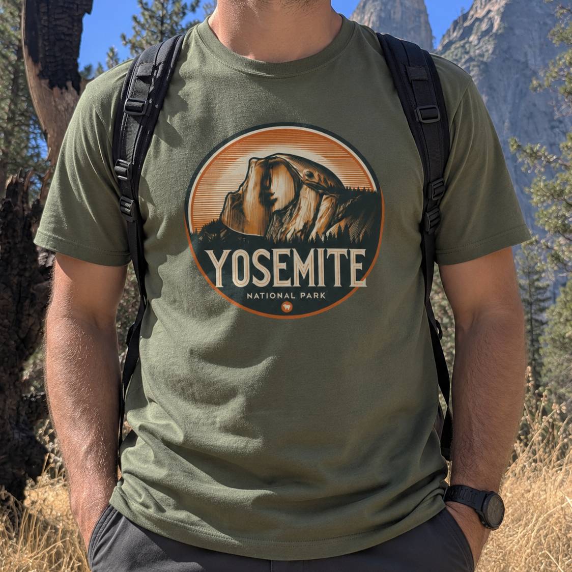 A man wearing an olive green t-shirt with a circular Yosemite National Park graphic on the chest, photographed outdoors in a mountain setting.