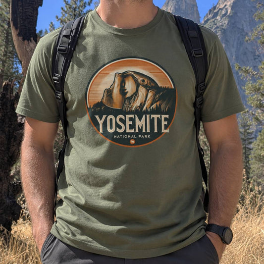 A man wearing an olive green t-shirt with a circular Yosemite National Park graphic on the chest, photographed outdoors in a mountain setting.
