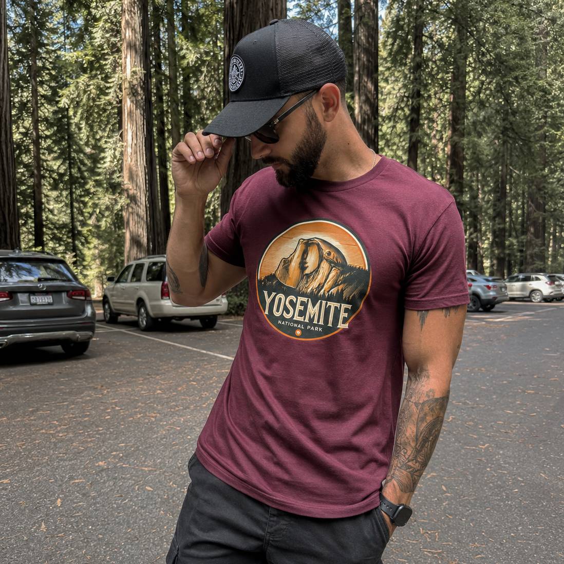 Man wearing a maroon t-shirt with Yosemite National Park logo in a forest setting.